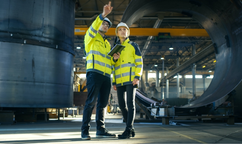 Construction project management software in use on site with male & female construction workers in protective wear.