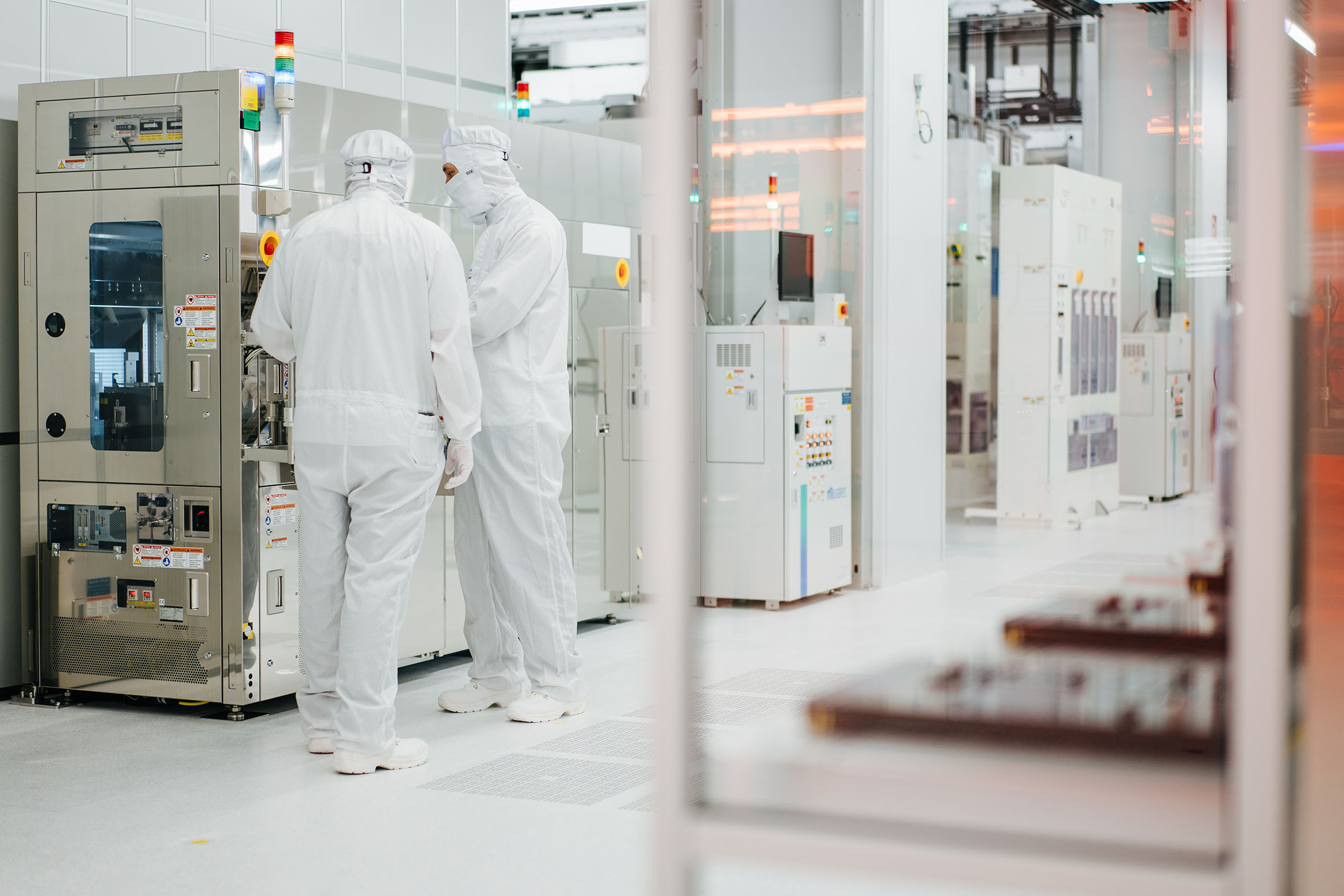 Inside large semiconductor fab in Austria showing two people in white sterile clothes with protective googles & head covering